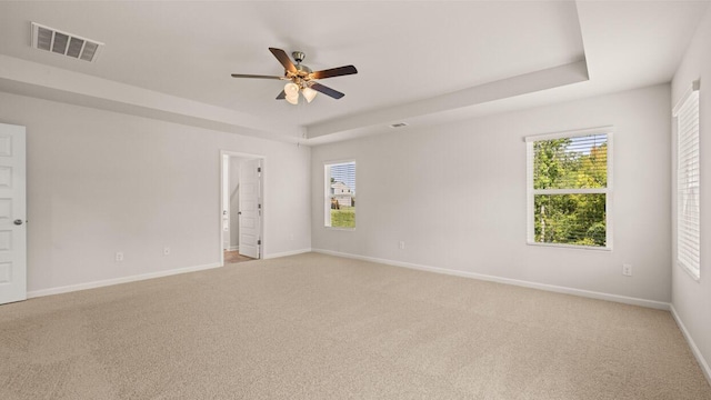 empty room with visible vents, light colored carpet, baseboards, and a tray ceiling