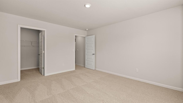 unfurnished bedroom with light carpet, a closet, a walk in closet, and baseboards