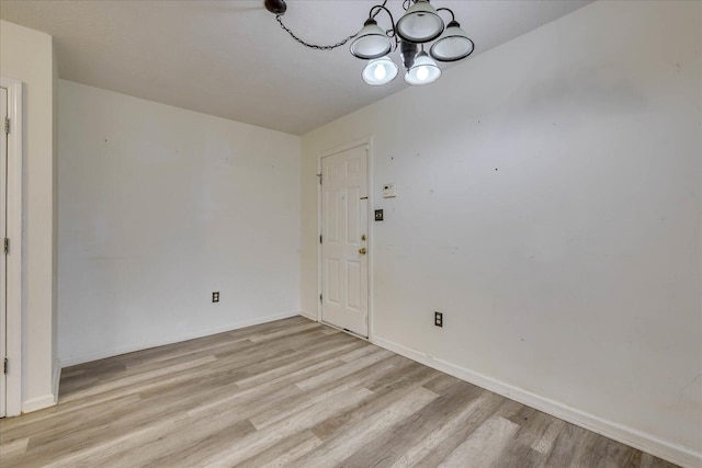 empty room with baseboards, light wood finished floors, and an inviting chandelier