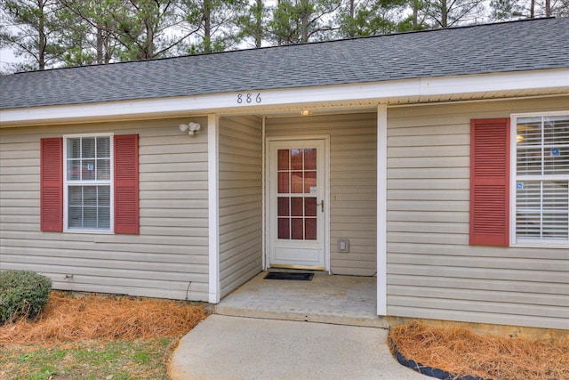 view of exterior entry with a shingled roof and a patio area