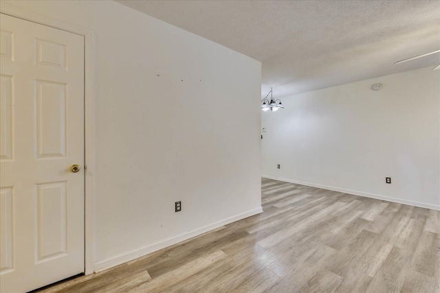 empty room featuring a chandelier, a textured ceiling, light wood-type flooring, and baseboards