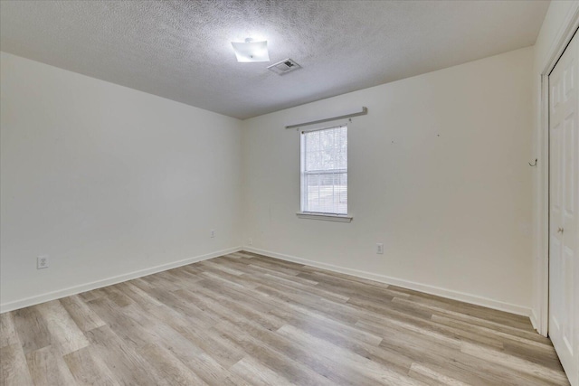 unfurnished room with a textured ceiling, light wood-type flooring, visible vents, and baseboards