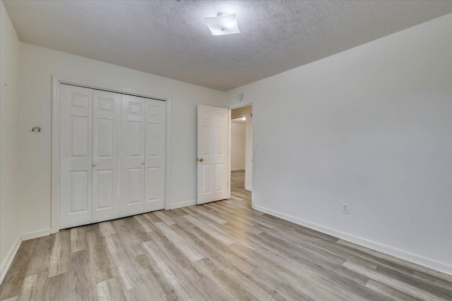 unfurnished bedroom featuring a textured ceiling, light wood-style flooring, and baseboards