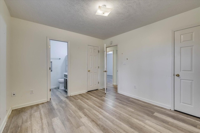 unfurnished bedroom featuring a textured ceiling, light wood-type flooring, ensuite bath, and baseboards