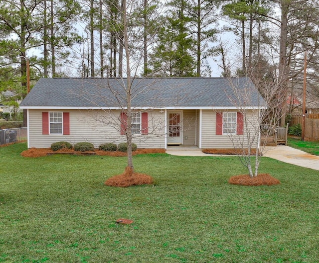 ranch-style home featuring a shingled roof, a front yard, and fence