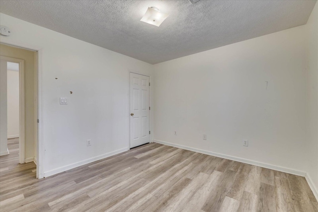 empty room with a textured ceiling, light wood-type flooring, and baseboards