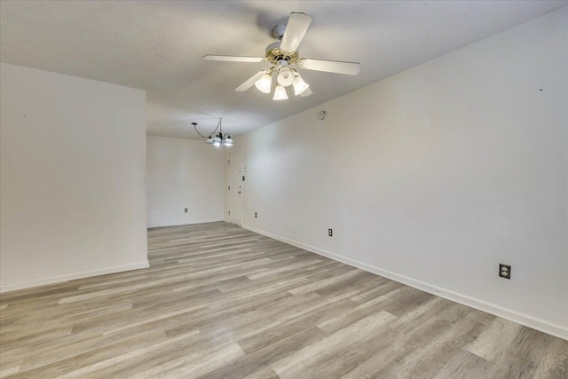 empty room featuring ceiling fan with notable chandelier, a textured ceiling, baseboards, and light wood-style floors