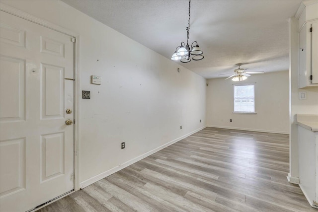 interior space featuring light wood-style floors, baseboards, a textured ceiling, and ceiling fan with notable chandelier