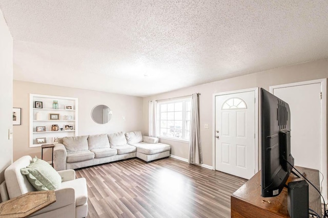 living area featuring baseboards, wood finished floors, a textured ceiling, and built in shelves