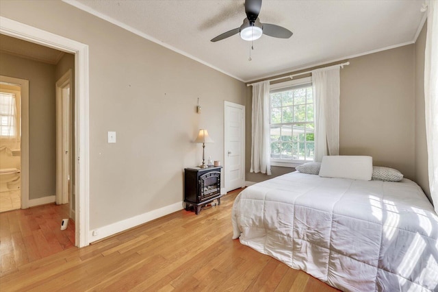 bedroom with a wood stove, crown molding, light hardwood / wood-style flooring, ceiling fan, and connected bathroom