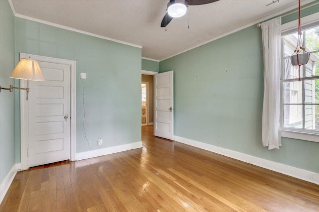 empty room featuring a wealth of natural light, crown molding, ceiling fan, and wood-type flooring