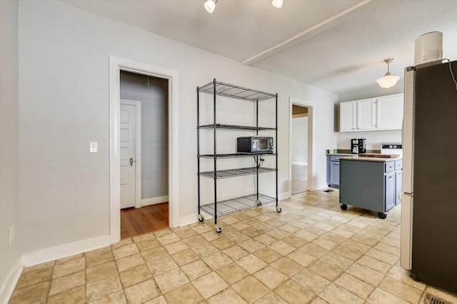 kitchen featuring stainless steel fridge, a textured ceiling, blue cabinetry, pendant lighting, and white cabinetry