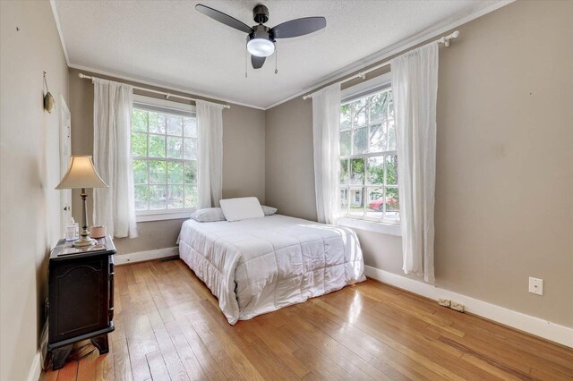 bedroom featuring ceiling fan, wood-type flooring, a textured ceiling, and ornamental molding