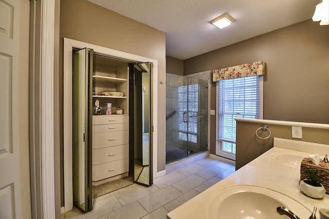 full bath with a sink, a textured ceiling, double vanity, and a shower stall