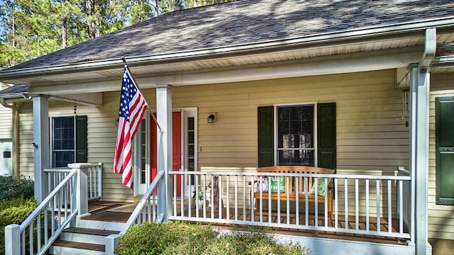 view of exterior entry with covered porch and roof with shingles