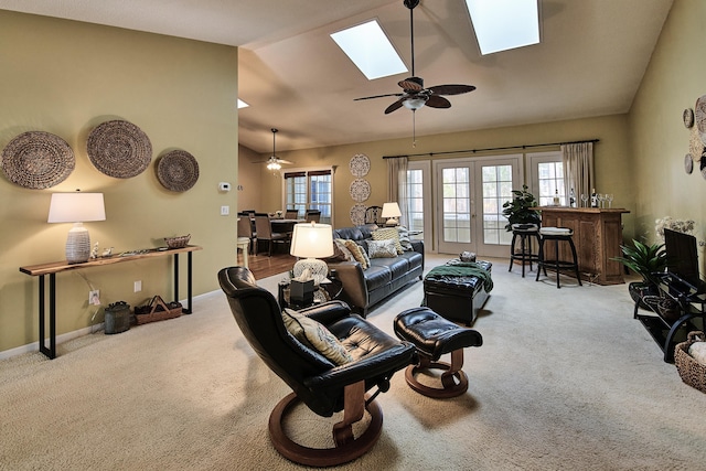 carpeted living area with french doors, lofted ceiling with skylight, baseboards, and ceiling fan