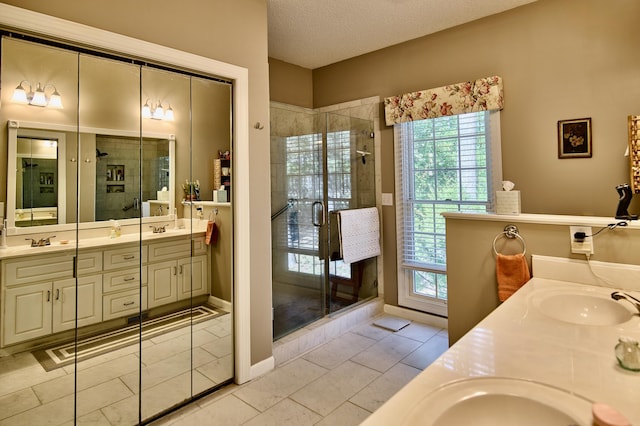 full bathroom with a textured ceiling, double vanity, a stall shower, and a sink