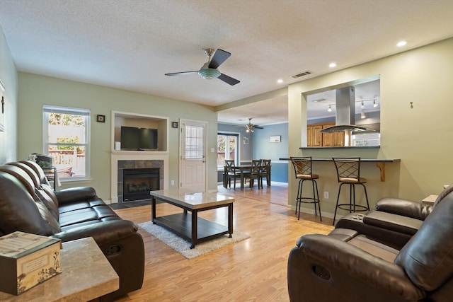 living room featuring a textured ceiling, light hardwood / wood-style flooring, ceiling fan, and a healthy amount of sunlight