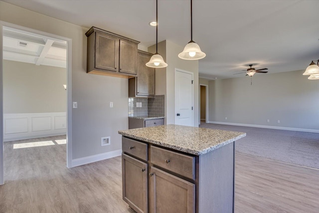 kitchen with a center island, hanging light fixtures, ceiling fan, light wood-type flooring, and light stone counters