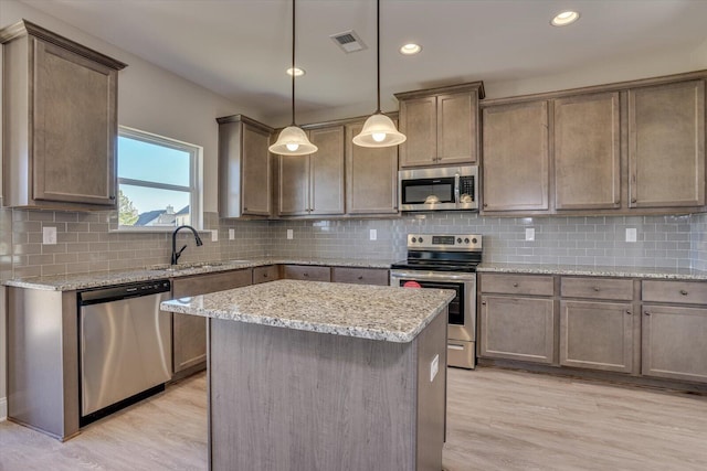 kitchen with light stone countertops, stainless steel appliances, pendant lighting, a center island, and light hardwood / wood-style floors