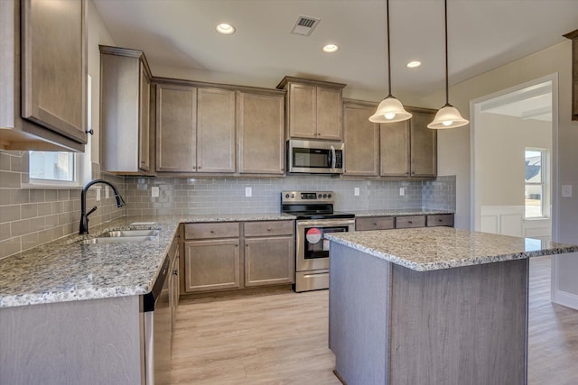 kitchen featuring decorative backsplash, stainless steel appliances, sink, light hardwood / wood-style floors, and hanging light fixtures