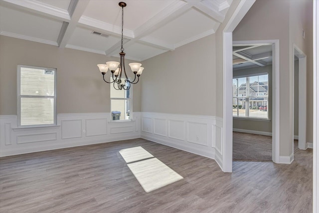 unfurnished dining area featuring beam ceiling, coffered ceiling, a notable chandelier, crown molding, and hardwood / wood-style flooring