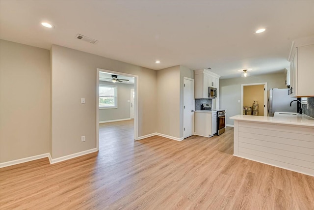 kitchen featuring stainless steel appliances, visible vents, white cabinets, light wood-style floors, and tasteful backsplash