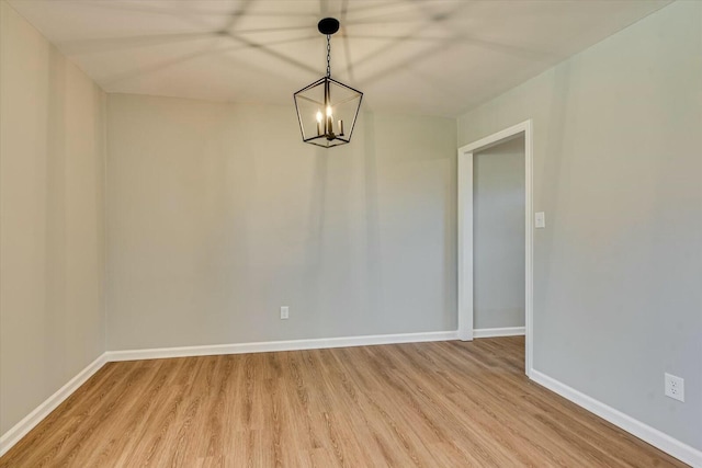 spare room featuring a chandelier, light wood finished floors, and baseboards