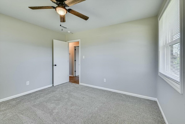 carpeted spare room featuring a ceiling fan and baseboards