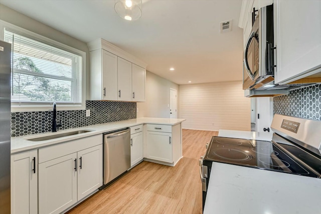 kitchen with light wood finished floors, visible vents, a peninsula, stainless steel appliances, and a sink