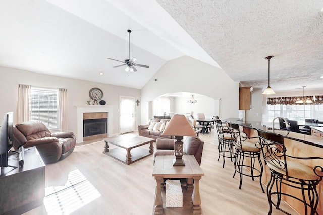 living room with ceiling fan, light hardwood / wood-style floors, a textured ceiling, and vaulted ceiling