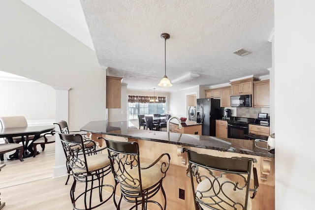 kitchen with a breakfast bar, black appliances, decorative light fixtures, light hardwood / wood-style floors, and kitchen peninsula