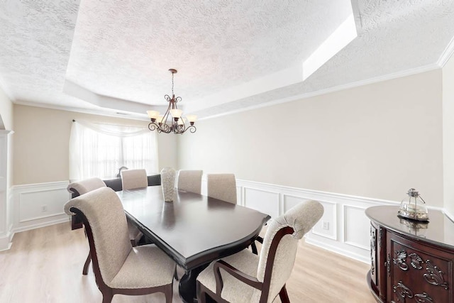 dining room featuring light wood-type flooring, a textured ceiling, a raised ceiling, crown molding, and an inviting chandelier