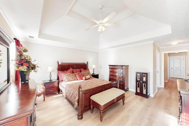 bedroom featuring a tray ceiling, ceiling fan, ornamental molding, and light wood-type flooring