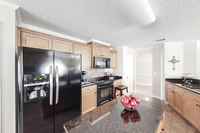 kitchen with black appliances, light tile patterned floors, ornamental molding, and dark stone counters