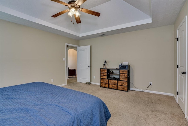 carpeted bedroom with a raised ceiling and ceiling fan