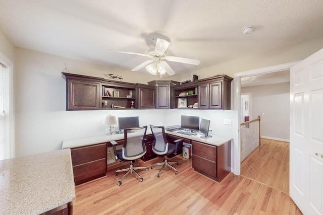 office area featuring baseboards, built in study area, light wood-style floors, and a ceiling fan