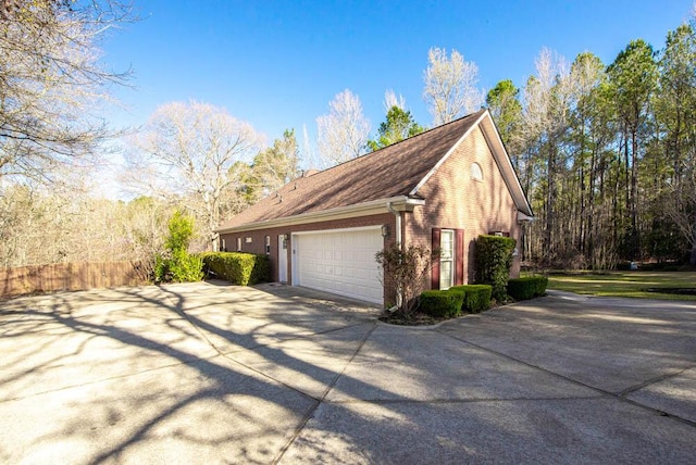 view of home's exterior featuring brick siding, driveway, an attached garage, and fence