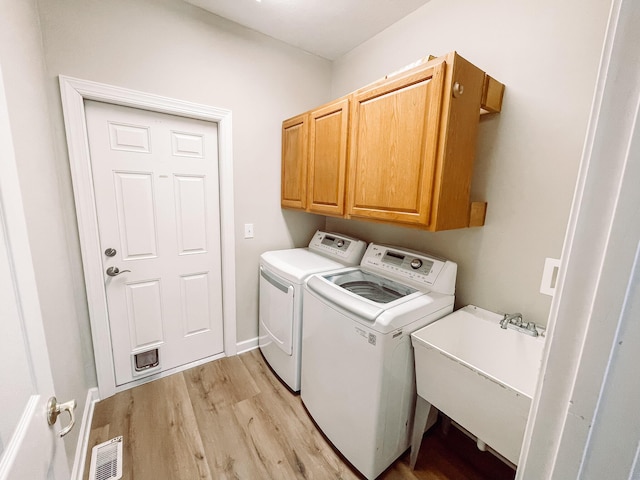 laundry area with a sink, visible vents, light wood-type flooring, independent washer and dryer, and cabinet space