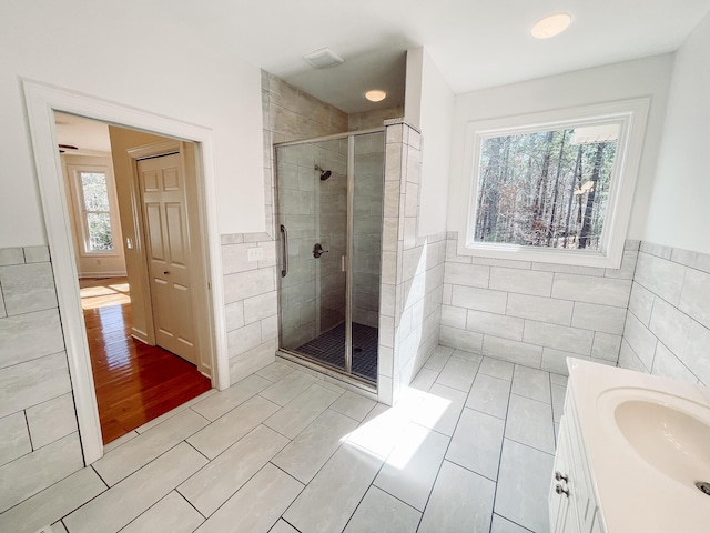 bathroom with a shower stall, vanity, tile walls, and wainscoting