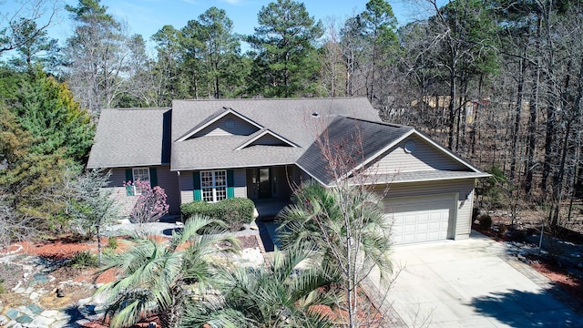 view of front of home with a shingled roof, driveway, a view of trees, and an attached garage