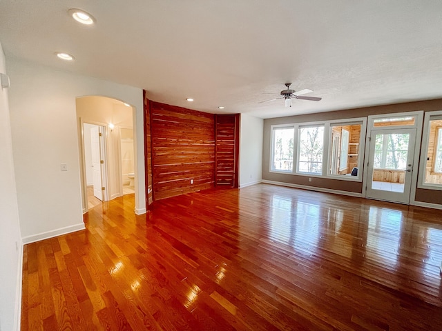 unfurnished living room with arched walkways, baseboards, wood finished floors, and recessed lighting