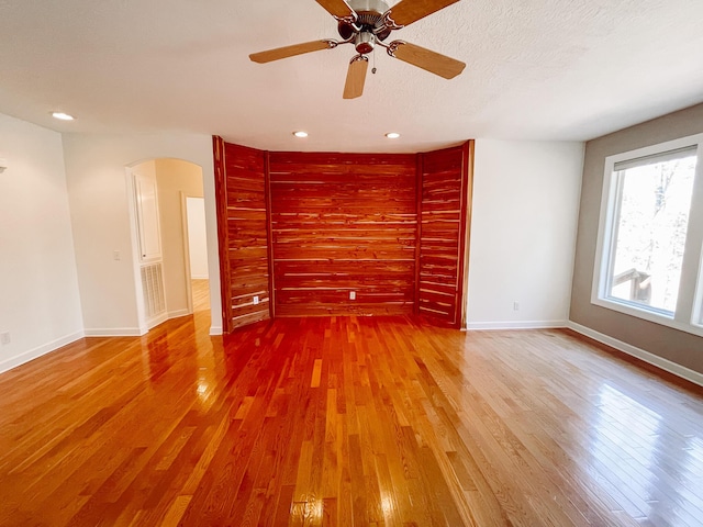 empty room featuring arched walkways, a textured ceiling, baseboards, and hardwood / wood-style flooring