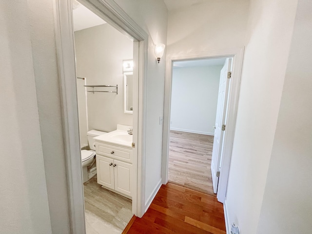 corridor with light wood-type flooring, baseboards, and a sink