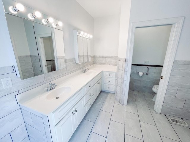 bathroom featuring double vanity, a sink, toilet, and tile walls