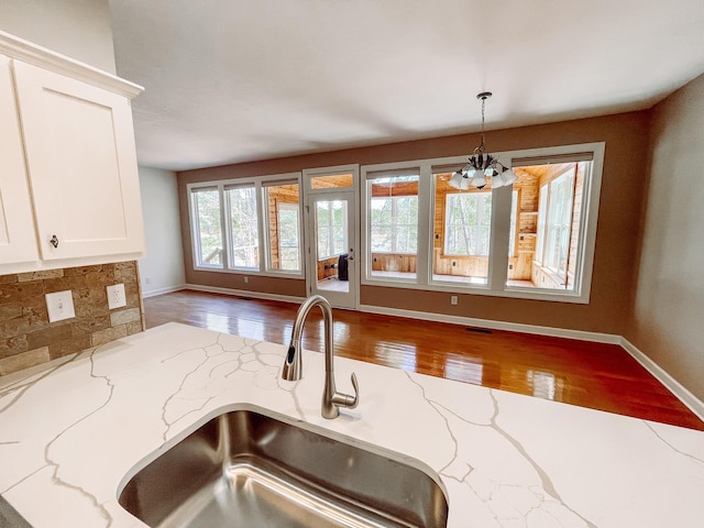 kitchen featuring light stone counters, pendant lighting, white cabinetry, a sink, and wood finished floors