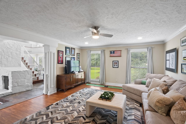 living room with wood finished floors, ornate columns, ornamental molding, ceiling fan, and stairway