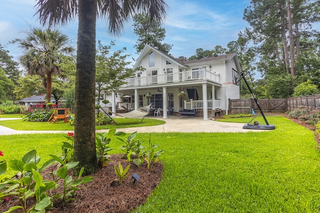 back of house featuring a balcony, a playground, a patio area, a lawn, and fence