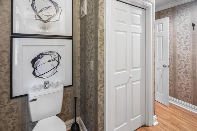 bathroom with baseboards, wallpapered walls, wood finished floors, and toilet