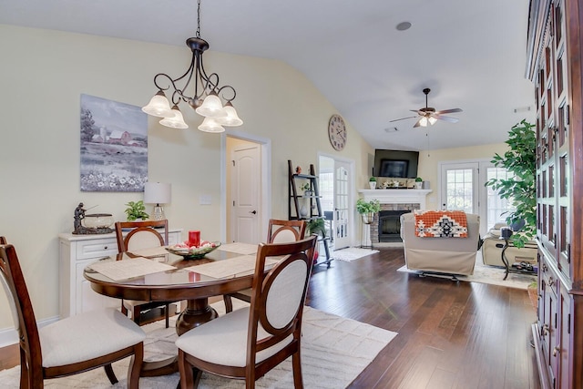 dining space featuring vaulted ceiling, a fireplace, dark wood finished floors, a ceiling fan, and a chandelier